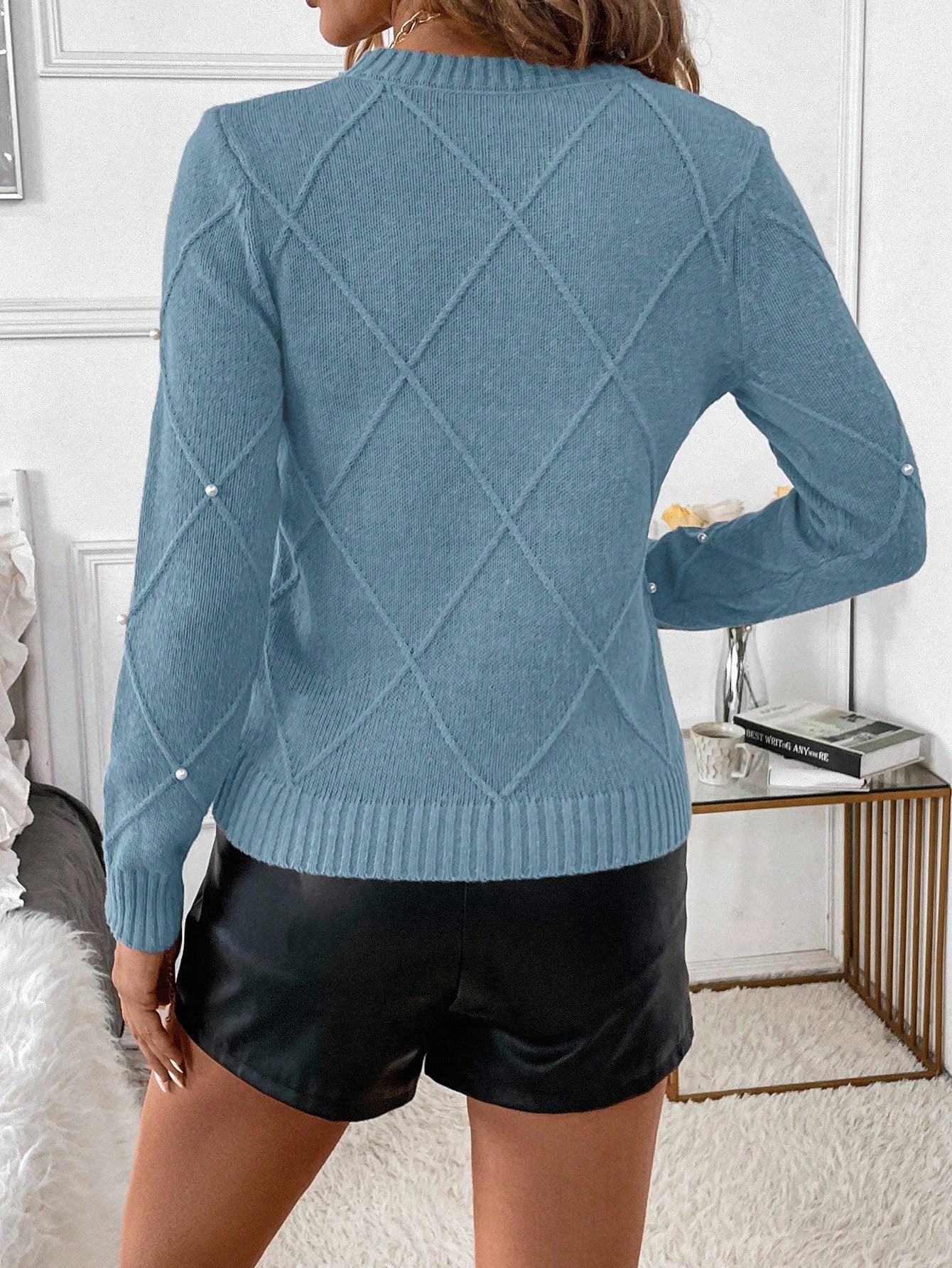 Person wearing a blue sweater with a diamond pattern and black shorts in an indoor setting.Nushes
