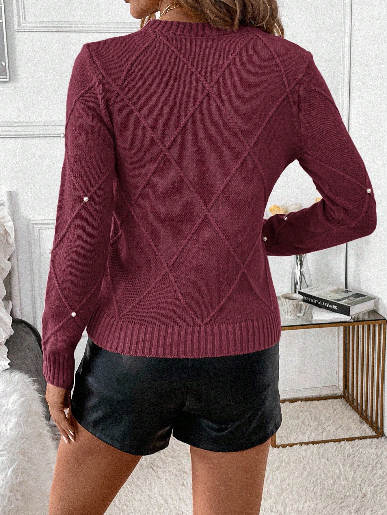 Person wearing a burgundy sweater with a diamond pattern and black shorts in an indoor setting.Nushes