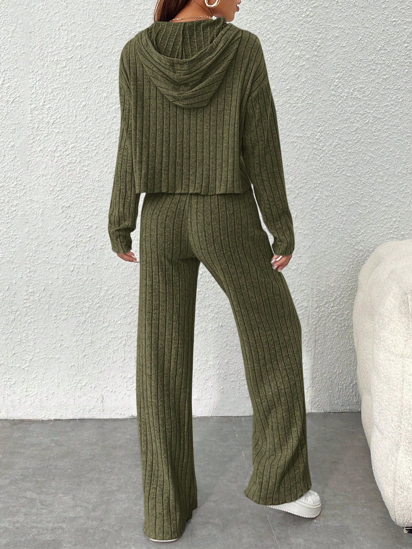 Person wearing a green ribbed knit hoodie and pants set against a white wall. Nushes