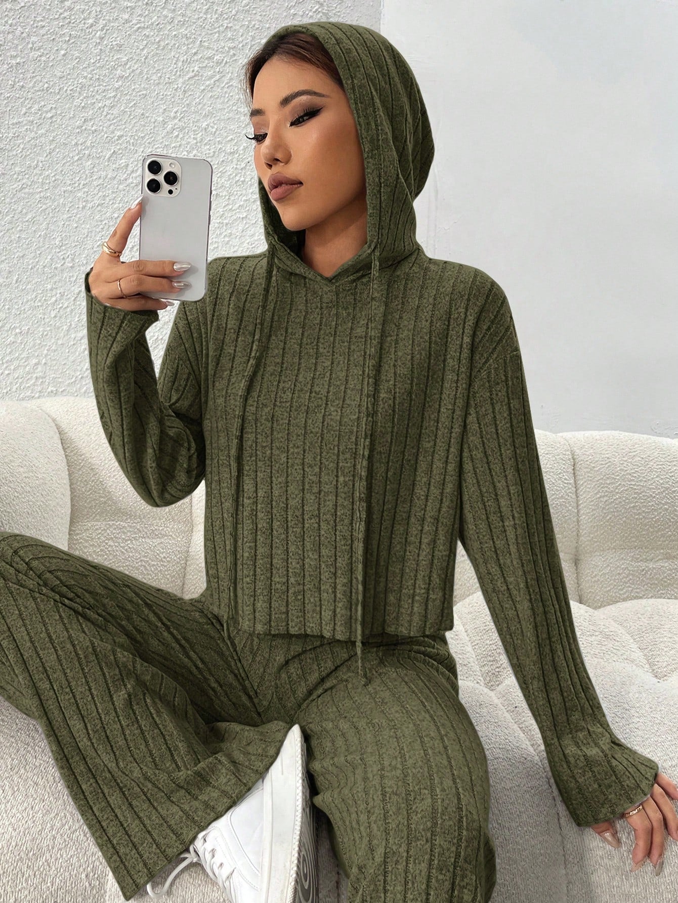 Person wearing a green ribbed knit outfit sitting on a white couch. Nushes