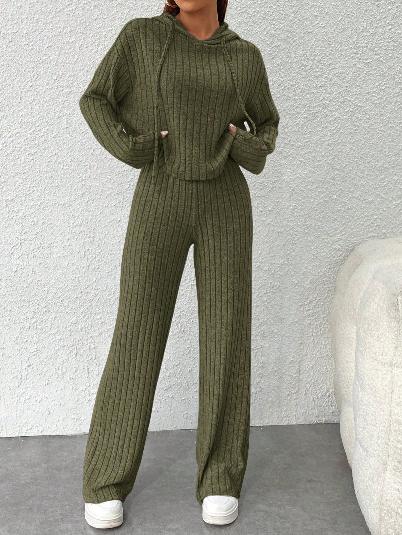 Person wearing an olive green ribbed sweater and pants set against a light gray background. Nushes