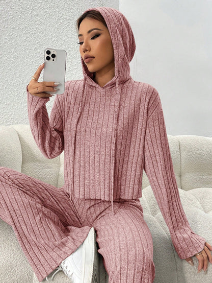 Person wearing a pink ribbed hoodie and pants sitting on a white couch. Nushes
