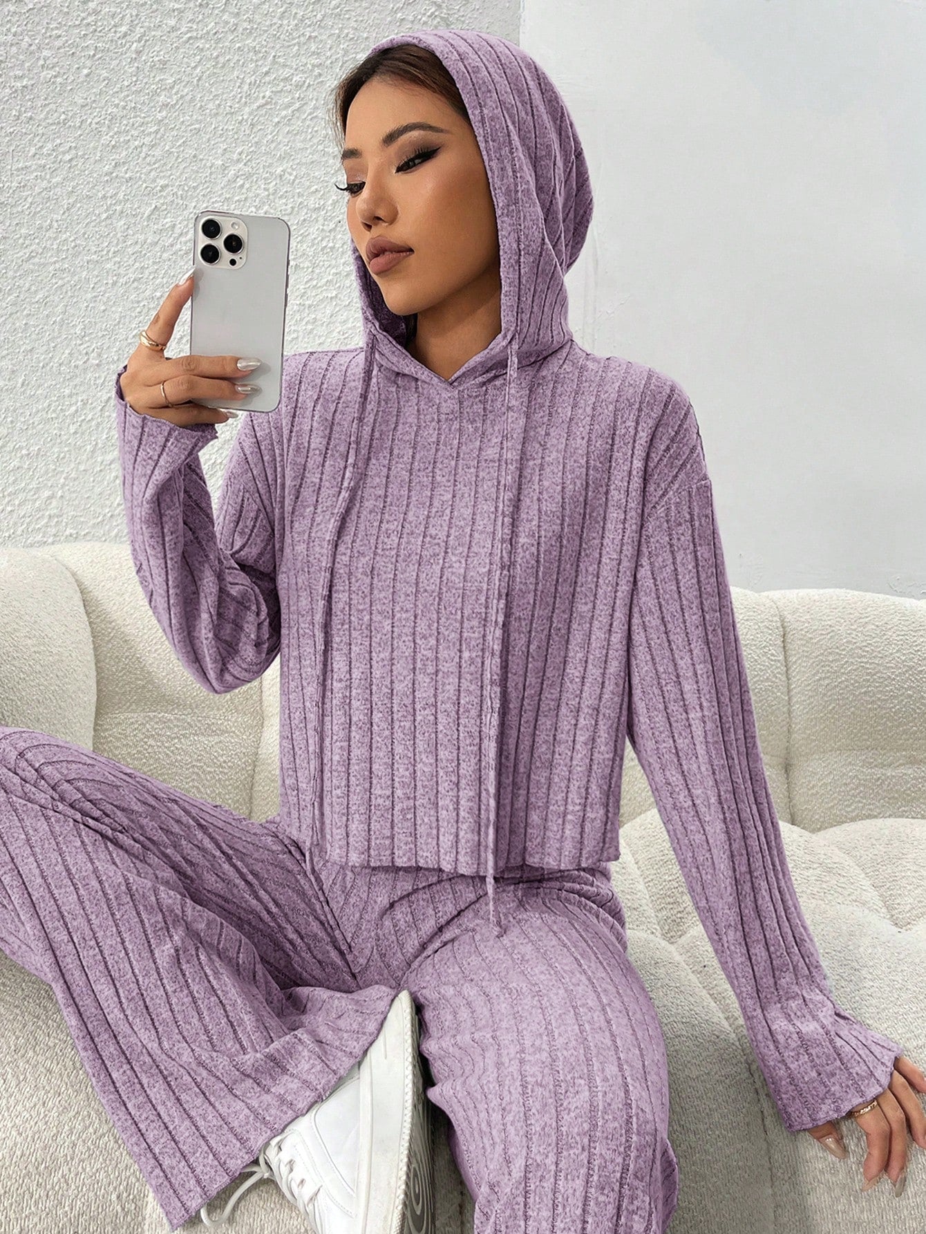 Person wearing a purple ribbed hoodie and pants sitting on a white couch. Nushes