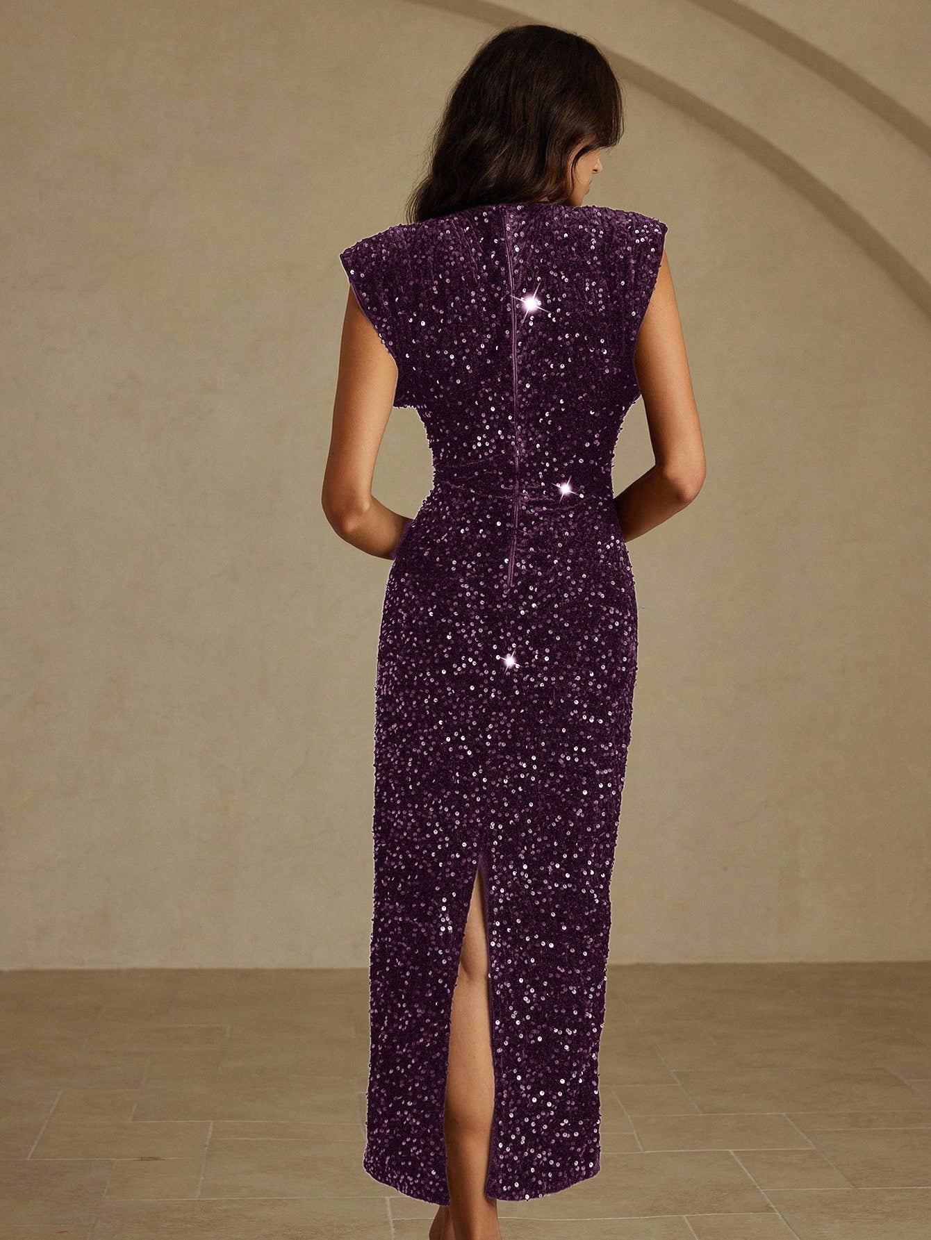 Woman wearing a purple sequin dress with a high slit on a beige background